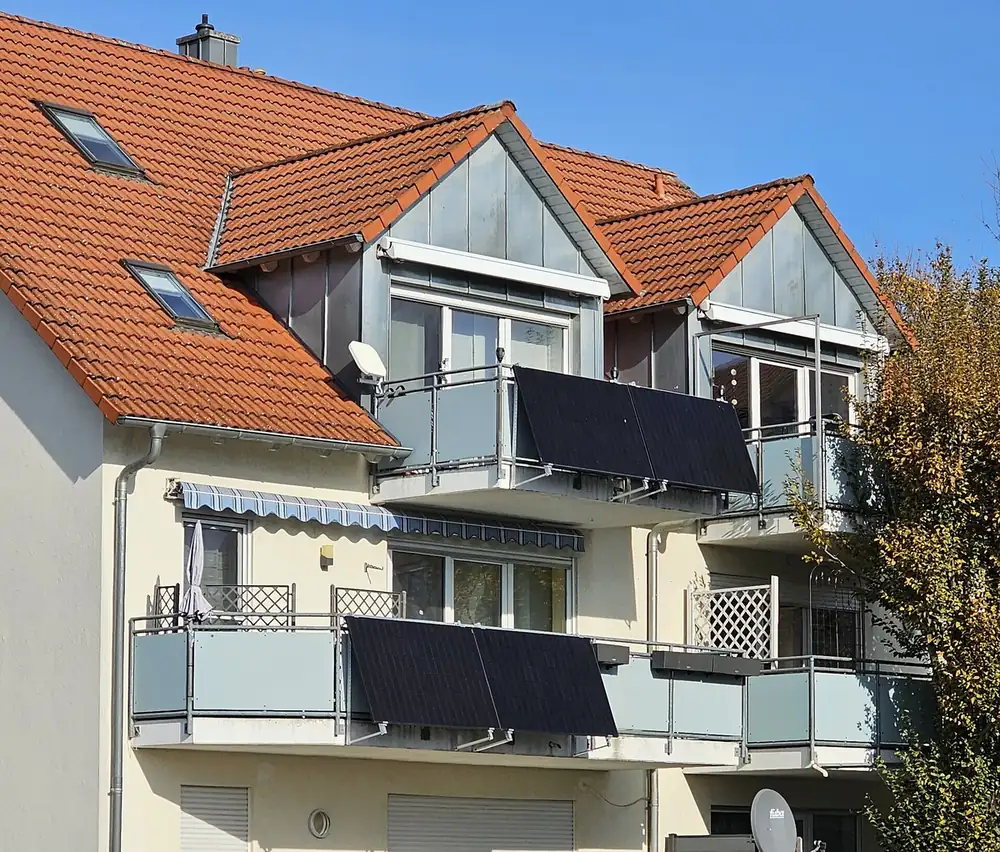 Dwa balkony domu, każdy z parą czarnych modułów fotowoltaicznych odchylonych na zewnątrz na wspornikach przy balustradzie