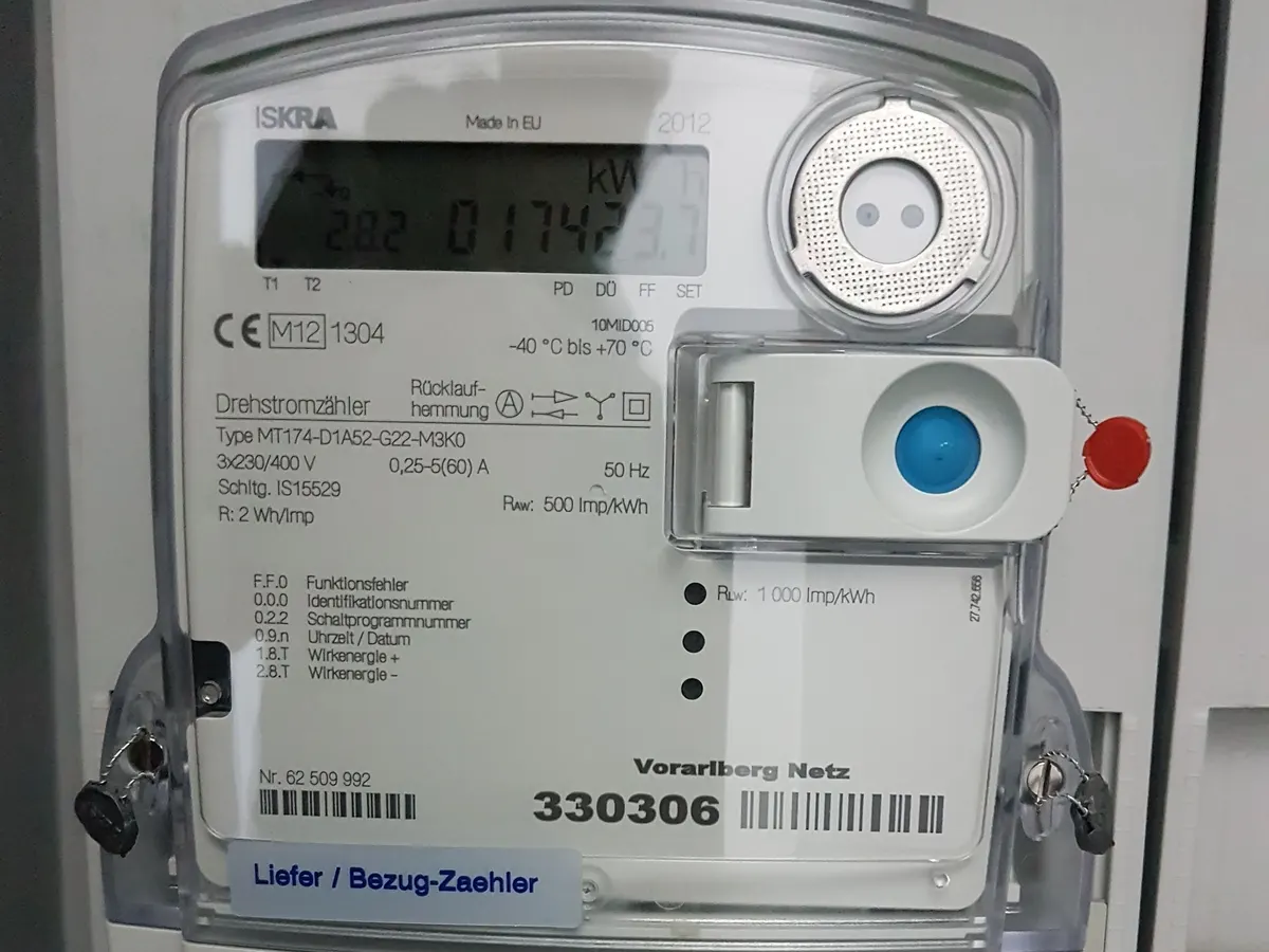 Szary trójfazowy licznik energii z ciekłokrystalicznym wyświetlaczem kWh, portem optycznym i etykietą Liefer / Bezug-Zaehler w domowej rozdzielnicy