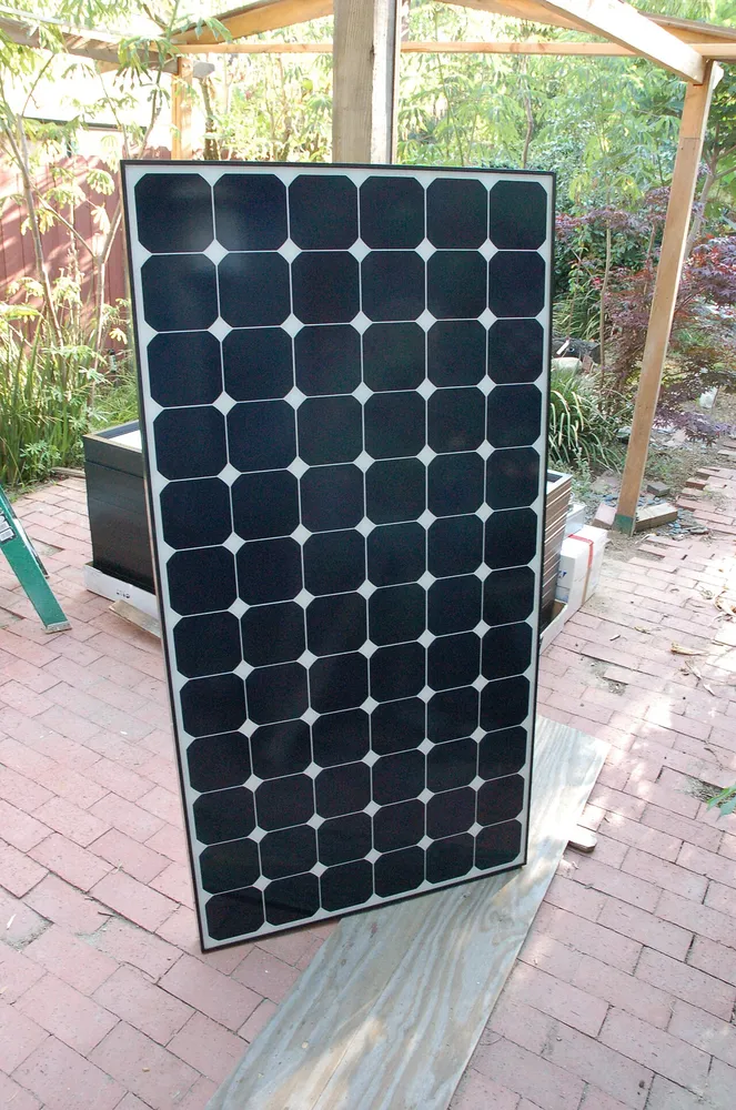 Moduł fotowoltaiczny SunPower oparty o pergolę w ogrodzie, czarne ogniwa ze ściętymi narożnikami bez żadnych srebrnych szyn i ścieżek na froncie