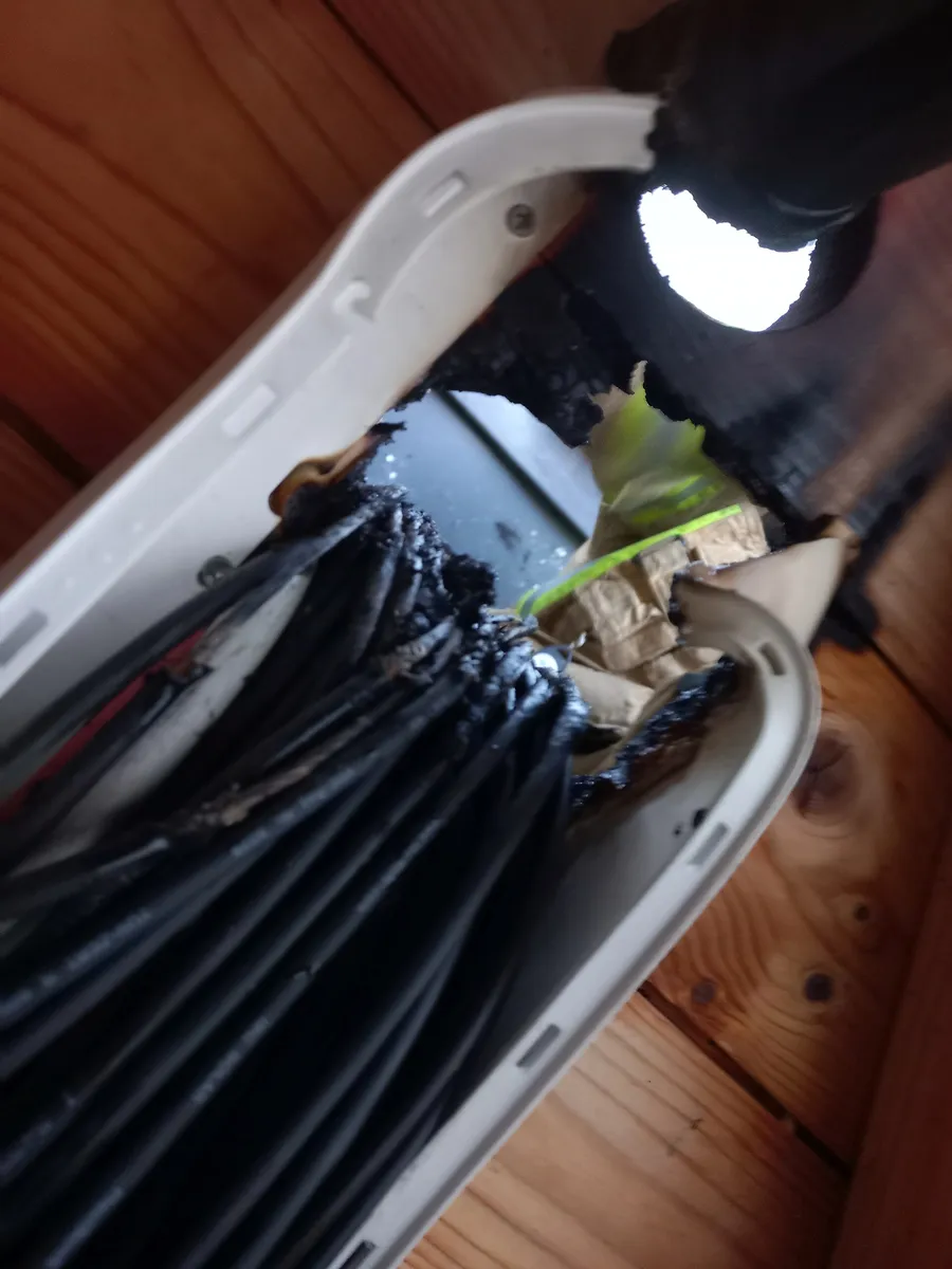 Nadpalona osłona z wiązką czarnych przewodów instalacji fotowoltaicznej po pożarze budynku