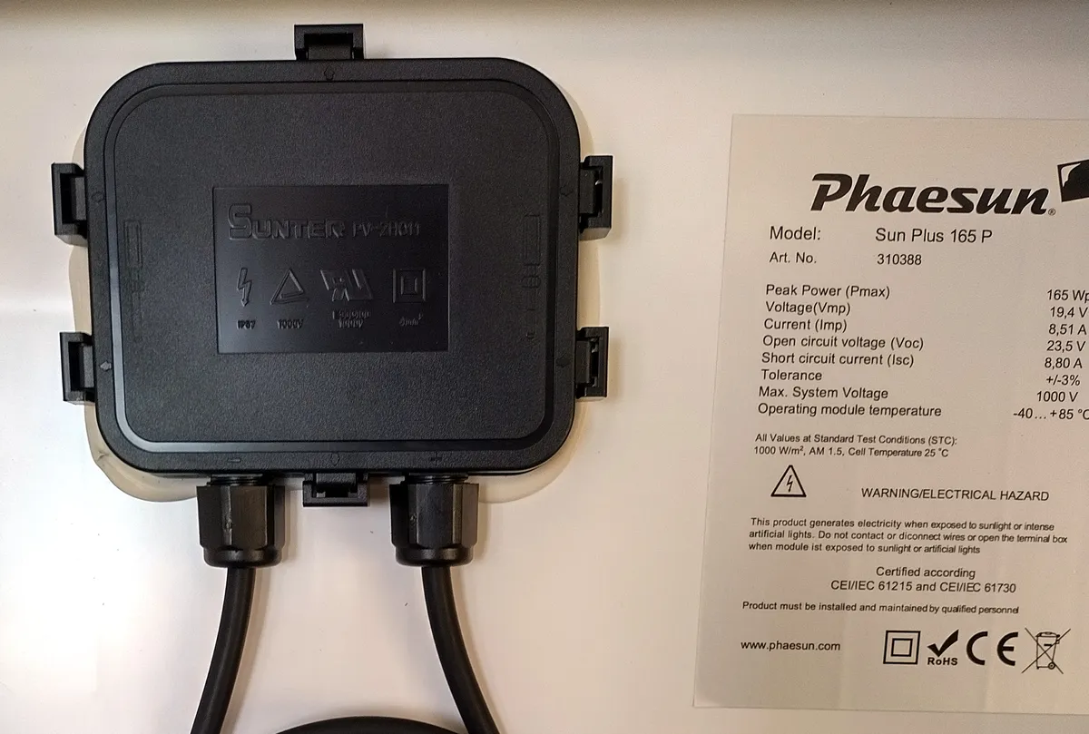 Tył małego modułu fotowoltaicznego z czarną puszką przyłączeniową obok białej tabliczki z napisem Certified according CEI/IEC 61215 i CEI/IEC 61730, nad rzędem znaków, wśród nich CE